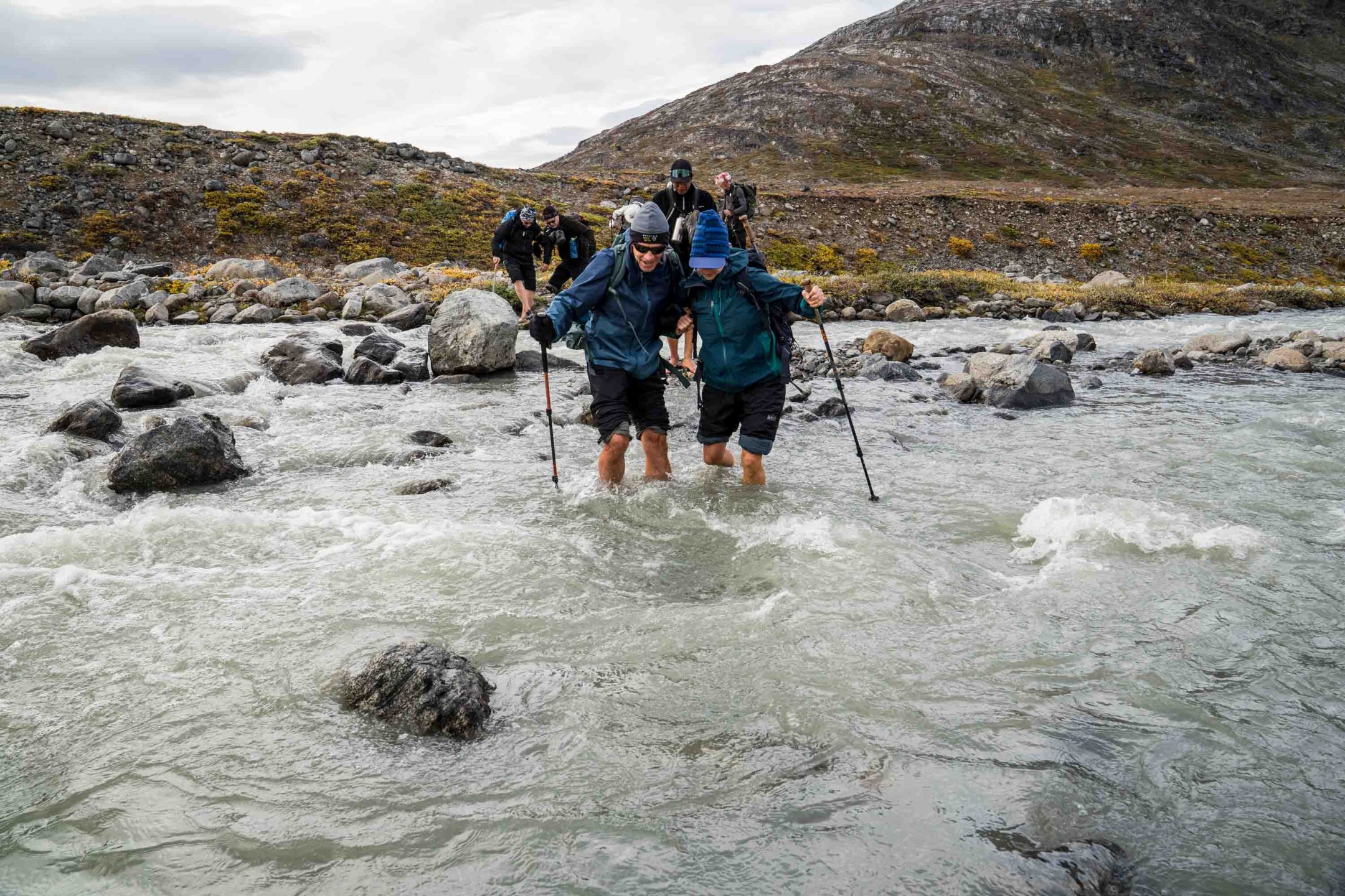 A group of hikers crossing a shallow Arctic river, carefully navigating the icy waters in East Greenland’s remote wilderness.