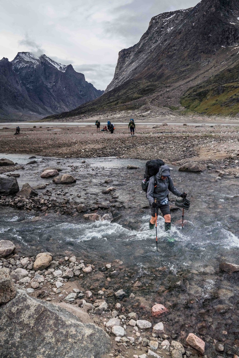 Group of hikers making their way along the Akshayuk Pass Trail, navigating a rocky river crossing.