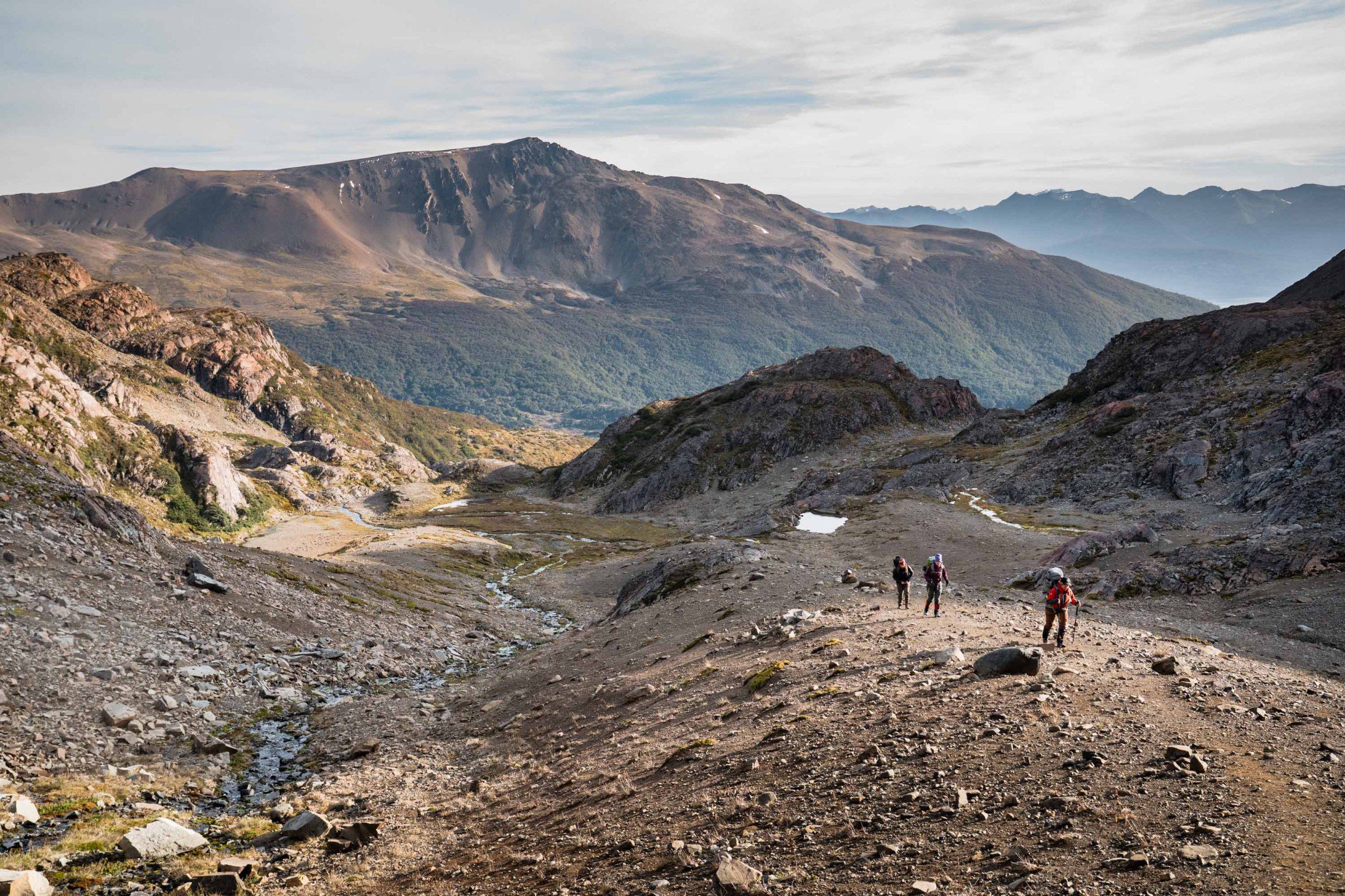 Hikers ascending a steep hillside on Day 2 of the Dientes de Navarino trek, surrounded by rocky alpine terrain in remote Patagonia.