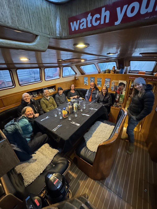 Expedition team gathered around the galley table onboard Ocean Tramp during an Antarctica sailing expedition