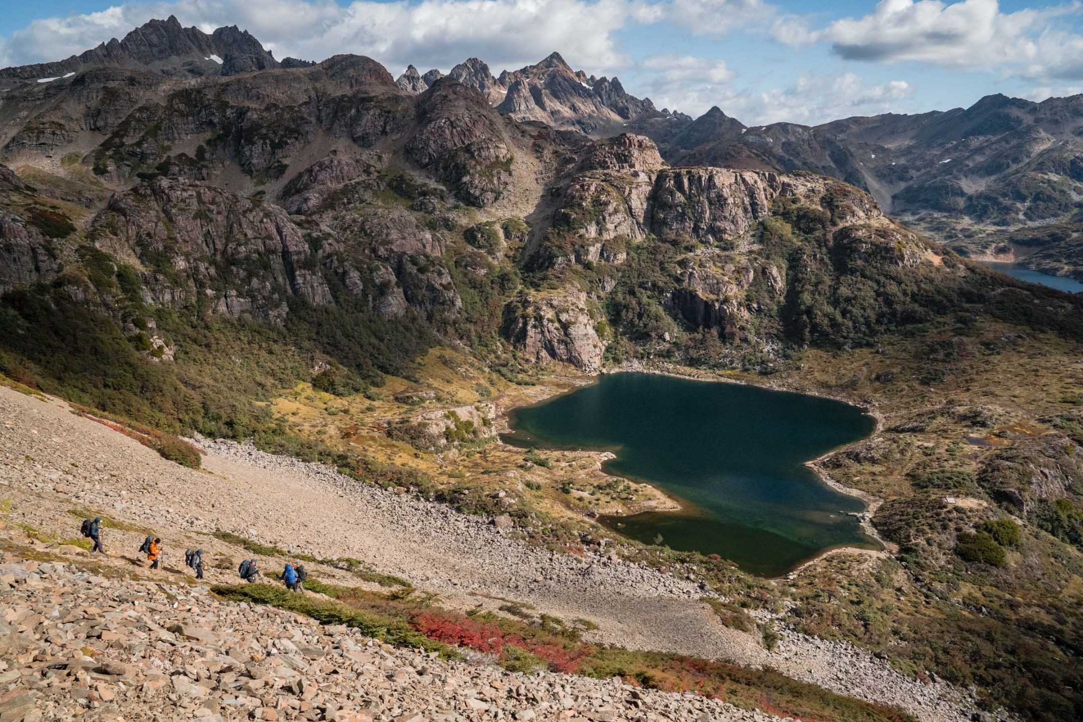 Hiker making their way along a remote trail in Patagonia, dwarfed by jagged mountain peaks and endless wilderness.