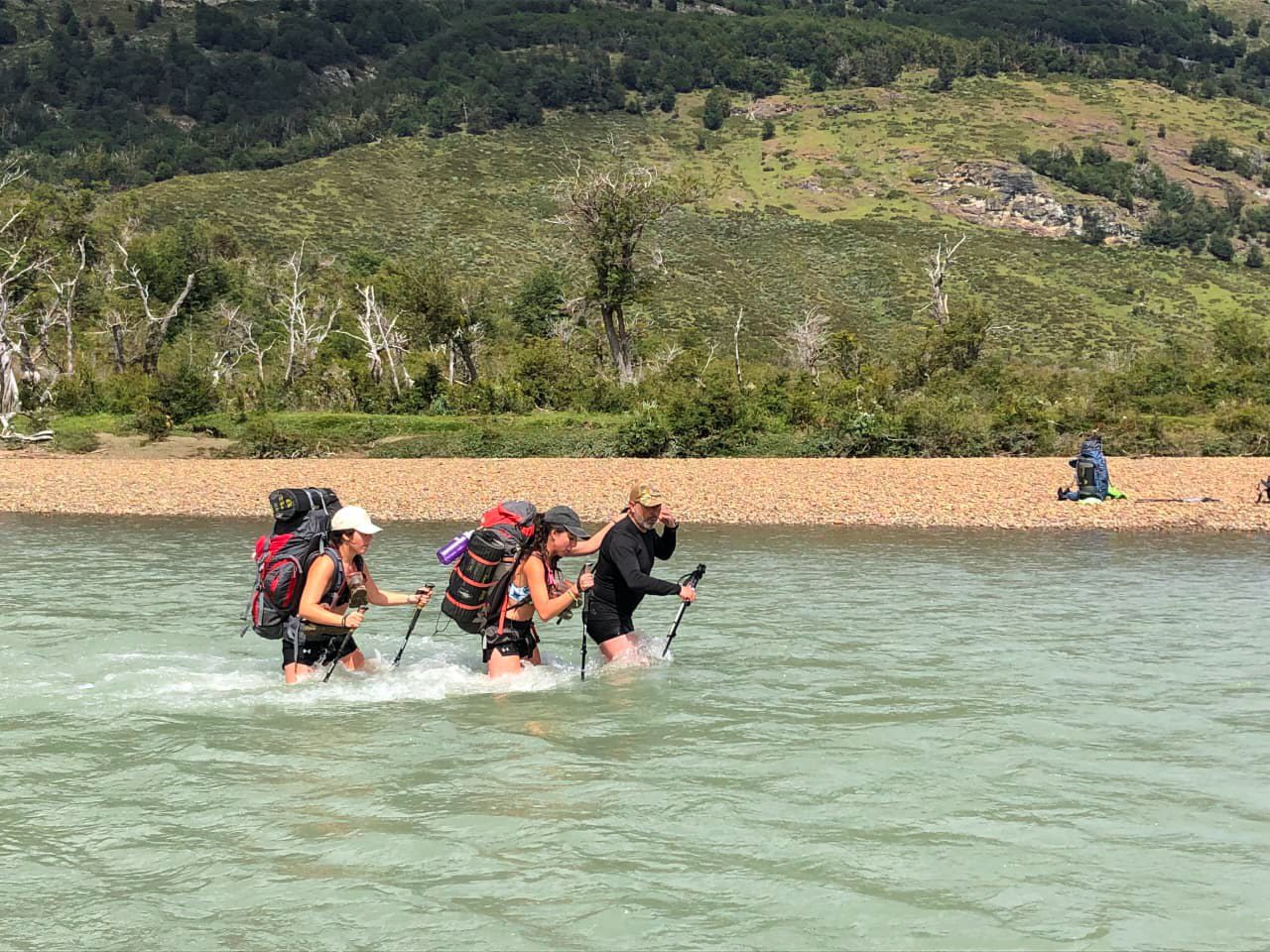 Three people crossing a glacial fed river in Yendegaia National Park.